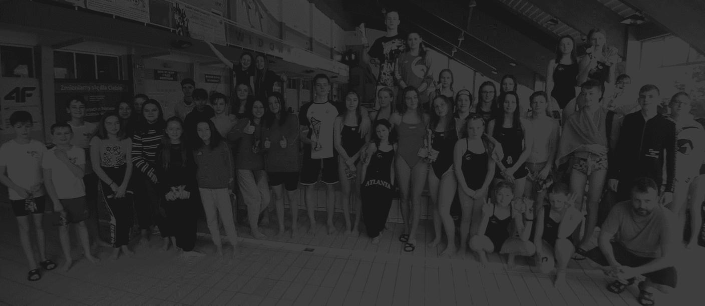 Liczna grupa zawodników Swimland Olsztyn z pucharami podczas wspólnego zdjęcia na hali basenowej