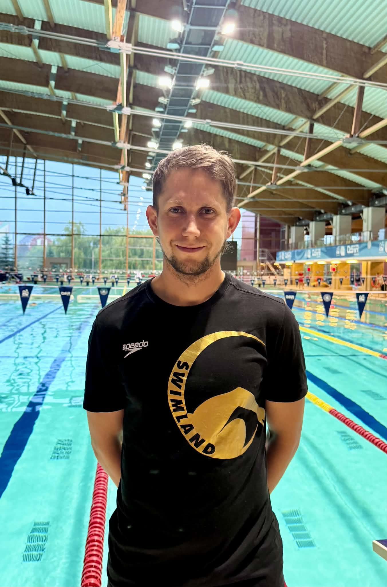 Paweł Najmowicz w czarnej koszulce Swimland na tle krytej pływalni
